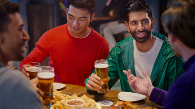 A group of men sitting around a table, drinking beer.