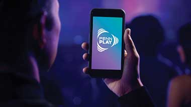 image of a person holding a phone displaying the PENN Play logo